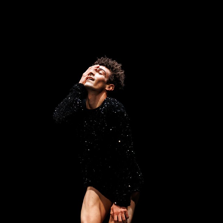 Tänzer in Kostüm auf der Bühne, der Boden ist schwarz und die Bühne ist professionell ausgeleuchtet.