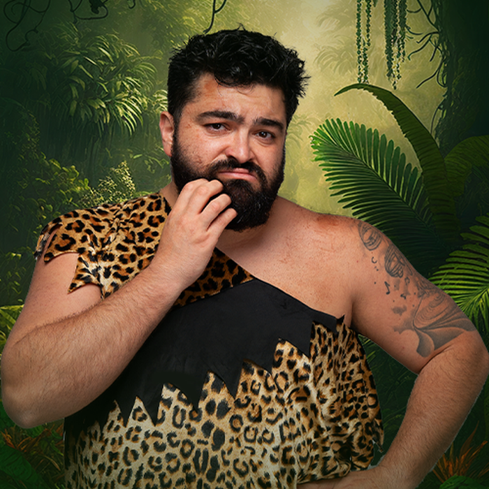 Ein Mann in einem Dschungel und einem Dschunger-Kostüm schaut fragend.