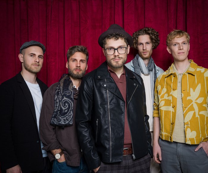 Die fünf Bandmitglieder von "anders" stehen vor einem roten Vorhang und blicken in die Kamera