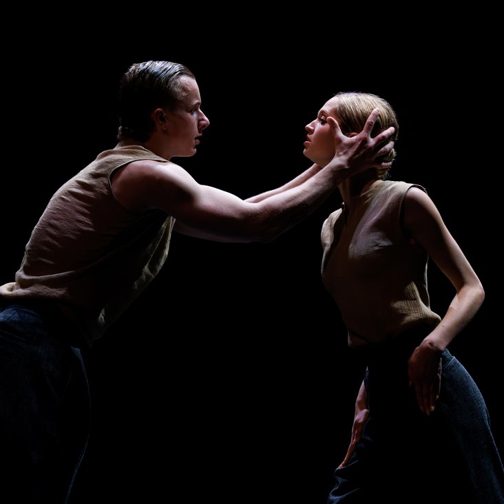 Tänzer:innen in Kostüm auf der Bühne, der Boden ist schwarz und die Bühne ist professionell ausgeleuchtet.