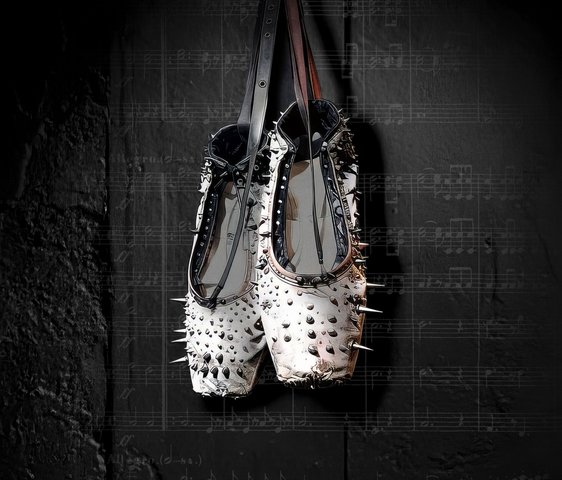 Ein Paar weißer Spitzenschuhe mit Nieten hängt vor einem schwarzen Hintergrund, der mit Musiknoten beschriftet ist.