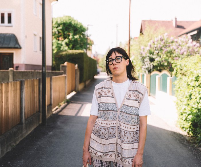 Eva Karl Faltermeier steht auf einer schmalen Straße in einem Wohngebiet, sie hält einen Stoffbeutel in der Hand.