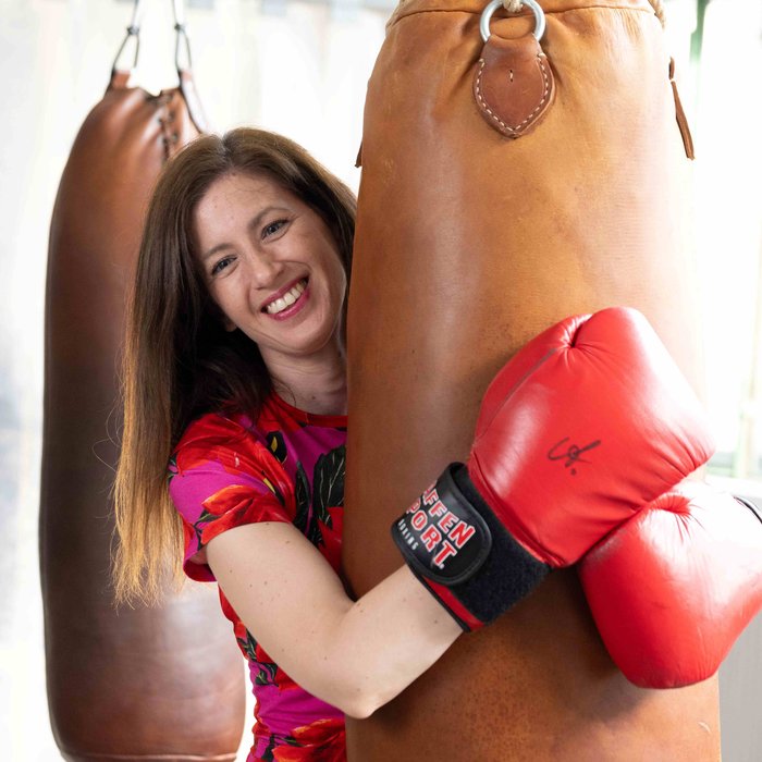 Claudia Pichler in rot-pinkem langem Kleid, sie trägt Boxhandschuhe und umarmt einen braunen Boxsack.