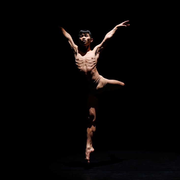 Tänzer in Kostüm auf der Bühne, der Boden ist schwarz und die Bühne ist professionell ausgeleuchtet.