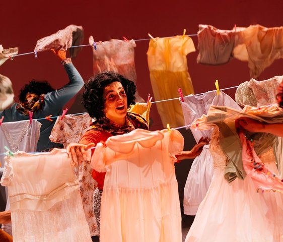 Drei Frauen hängen auf der Bühne bunte Kleidungsstücke auf eine Wäscheleine