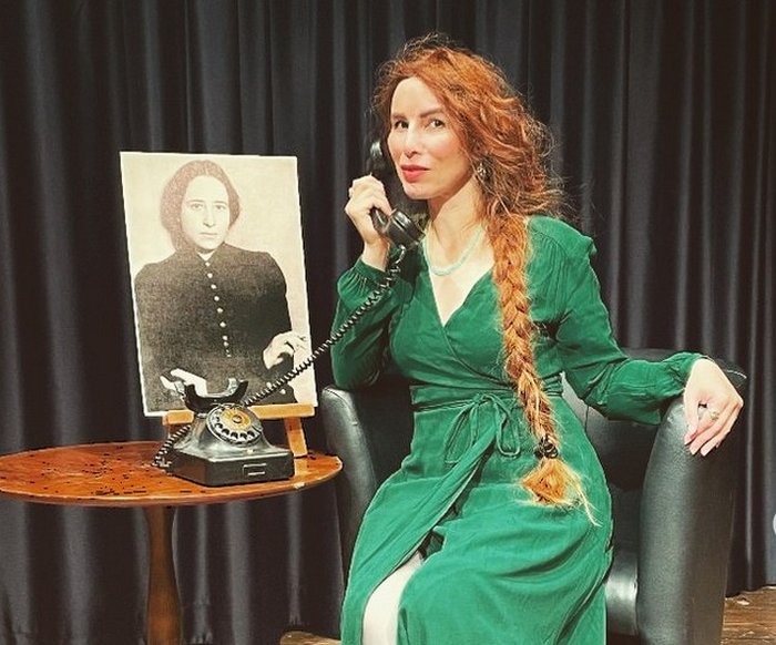 Eine Frau sitzt auf einem Sessel und hat ein altes Schnurtelefon am Ohr.