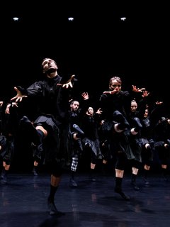 Die Tänzer:innen von Gauthier Dance in schwarzen Kostümen auf der Bühne. Die Bühne ist auch dunkel und es gibt wenig Licht.