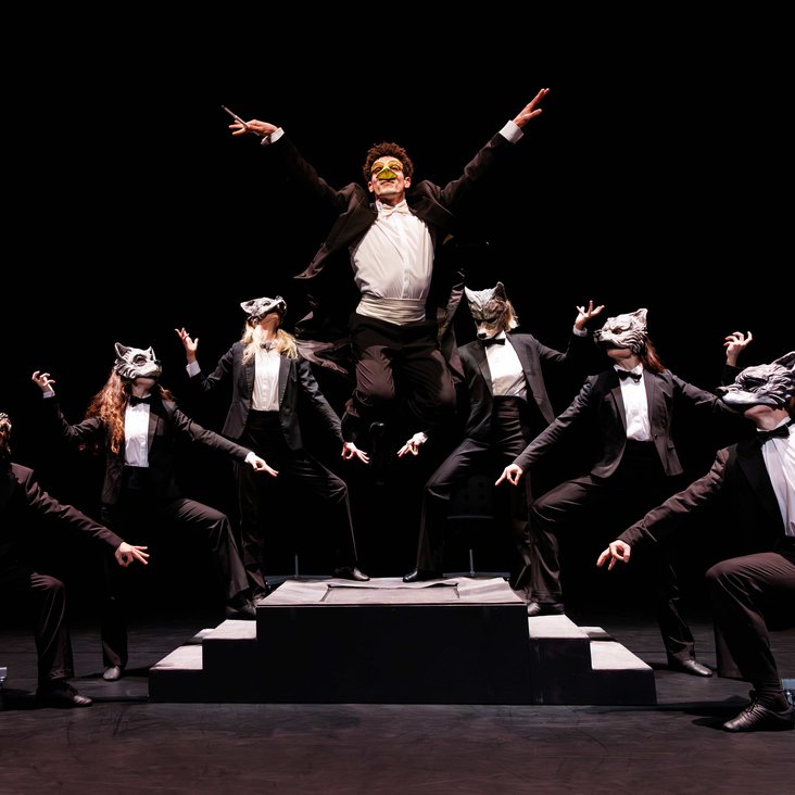 Tänzer:innen in Kostüm auf der Bühne, der Boden ist schwarz und die Bühne ist professionell ausgeleuchtet.