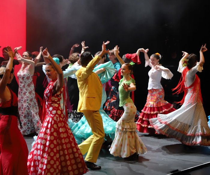 Mehrere Flamencotänzer:innen in bunten Kleidern auf einer Bühne, wie sie tanzen