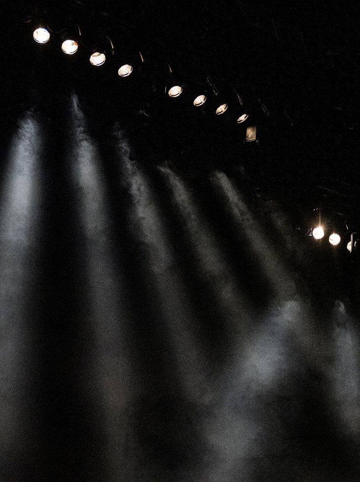 Bühnenlicht auf einer Bühne. Der Hintergrund ist schwarz, die Bühnenleuchten strahlen in kühlem weiß.