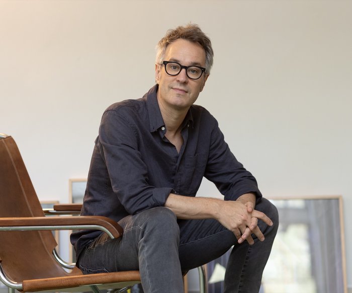 Porträt eines Komponisten im Sitzen in einem hellen Raum, entspannte, nachdenkliche Haltung.