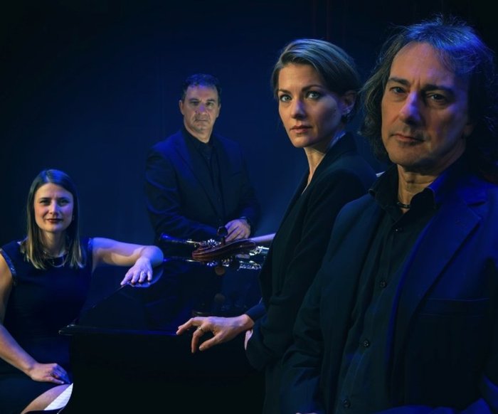 Das Quartett schaut in die Kamera, der Hintergrund ist schwarz und die Beleuchtung blau.