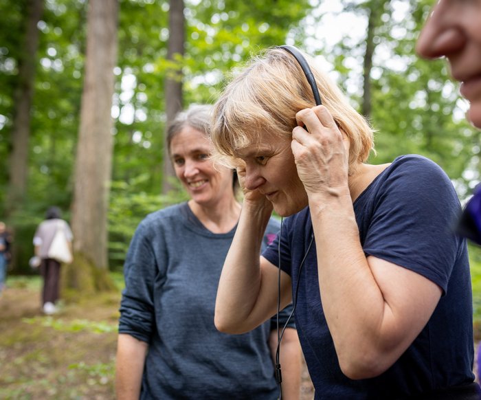 Teilnehmende einer Musikveranstaltung im Wald, Menschen hören Klängen über Kopfhörer in natürlicher Umgebung zu.
