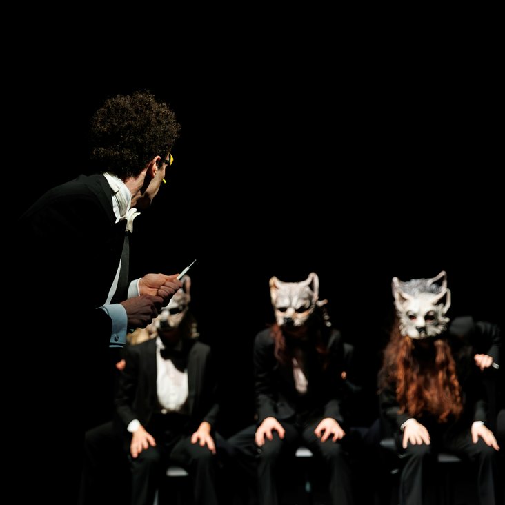 Tänzer:innen in Kostüm auf der Bühne, der Boden ist schwarz und die Bühne ist professionell ausgeleuchtet.