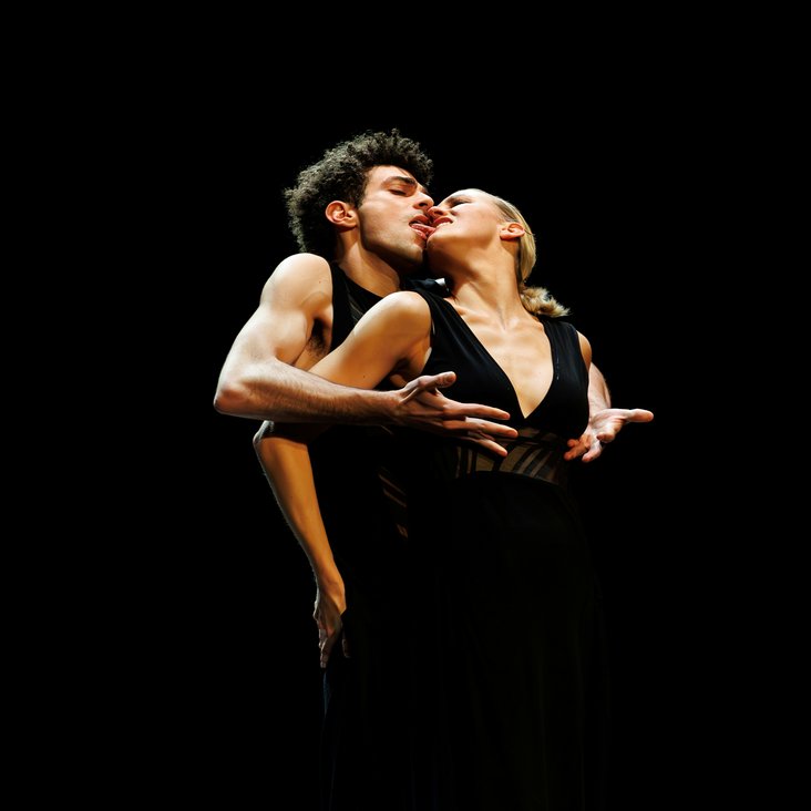 Tänzer:innen in Kostüm auf der Bühne, der Boden ist schwarz und die Bühne ist professionell ausgeleuchtet.