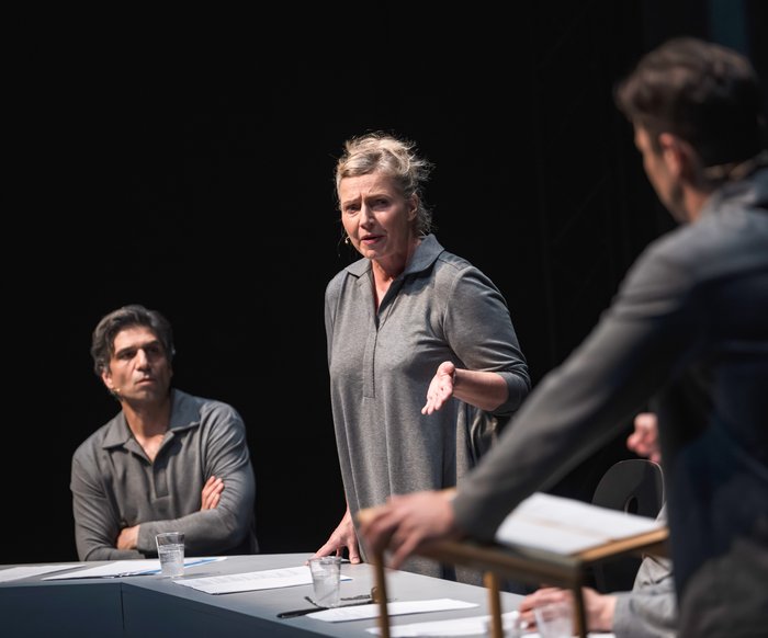 Szenenfoto, es zeigt drei Schauspieler:innen, die grau gekleidet sind, auf der Bühne