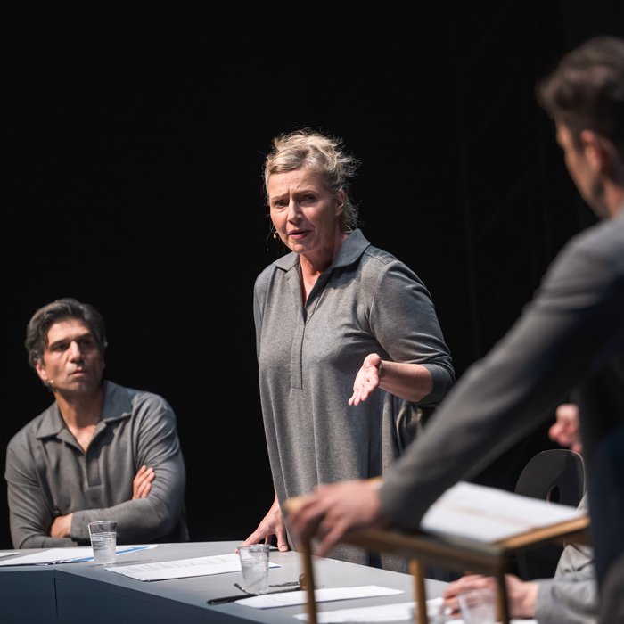 Szenenfoto, es zeigt drei Schauspieler:innen, die grau gekleidet sind, auf der Bühne