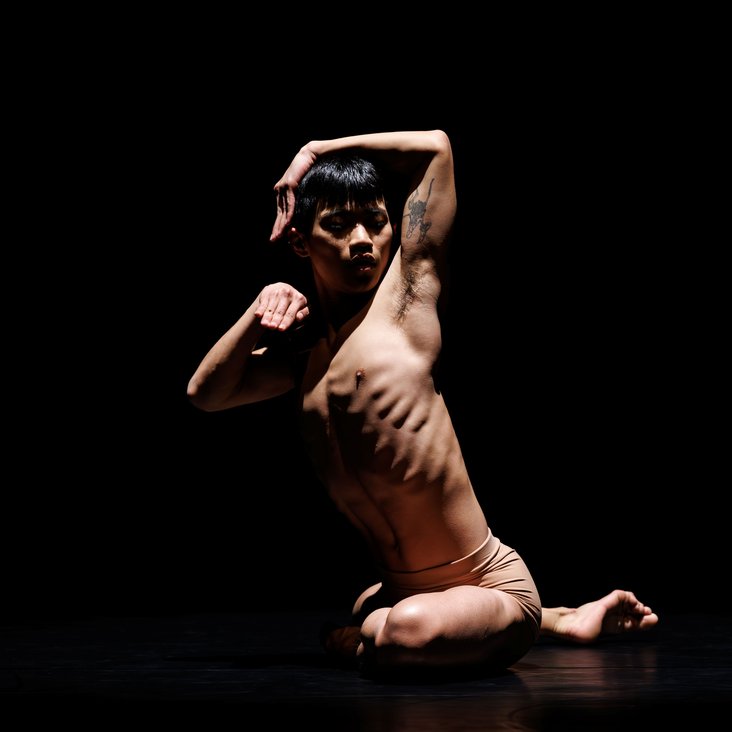 Tänzer in Kostüm auf der Bühne, der Boden ist schwarz und die Bühne ist professionell ausgeleuchtet.