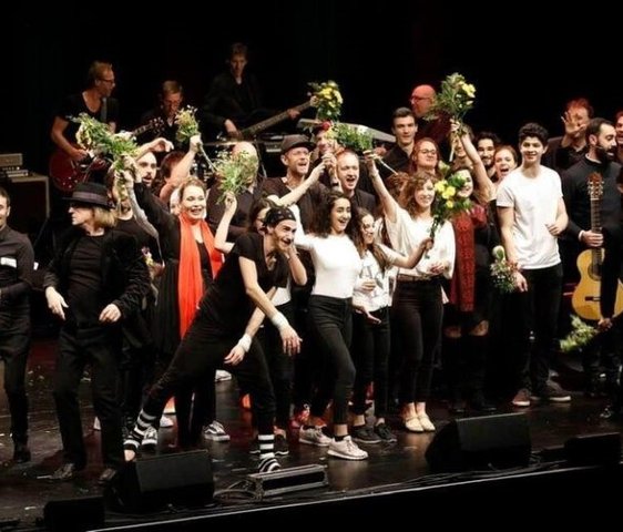 Eine Gruppe an Künstler:innen verteilt Blumen auf einer Bühne.