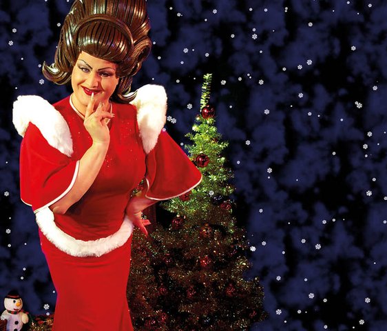 Die Künstler:in steht schmunzelnd vor einem Weihnachtsbaum